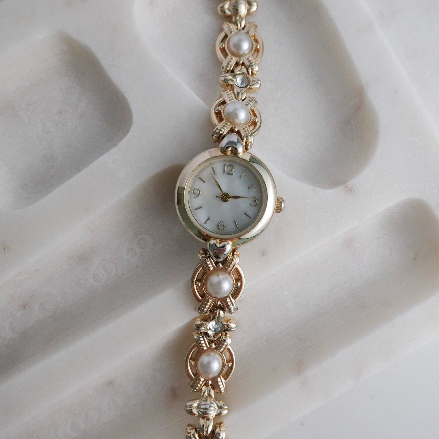 Gold bracelet watch with pearl-like beads on a marble surface